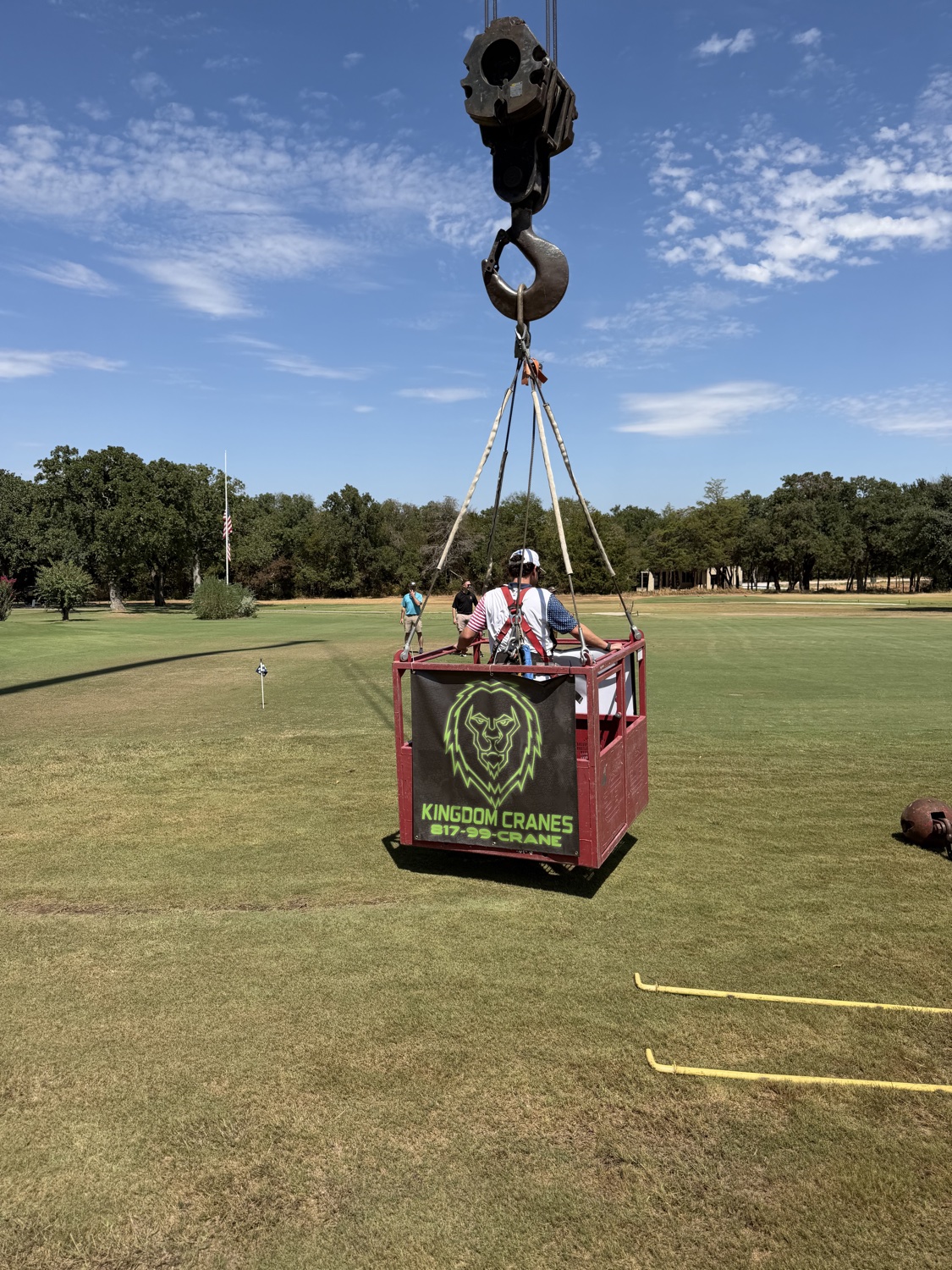 Kingdom Cranes operator riding in a man-basket suspended from a crane over a golf course